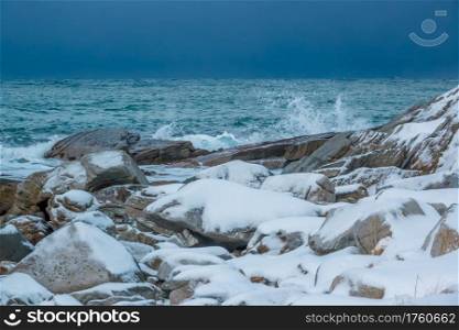 Calm ocean. Snow-covered rocky shore. Early winter. Heavy overcast sky above the horizon. Snow-Covered Stones on the Shore of a Calm Ocean