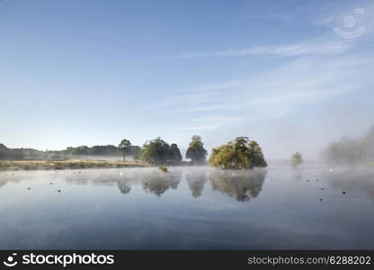 Calm peaceful lake with mist hanging over water on frosty Autumn Fall morning landscape