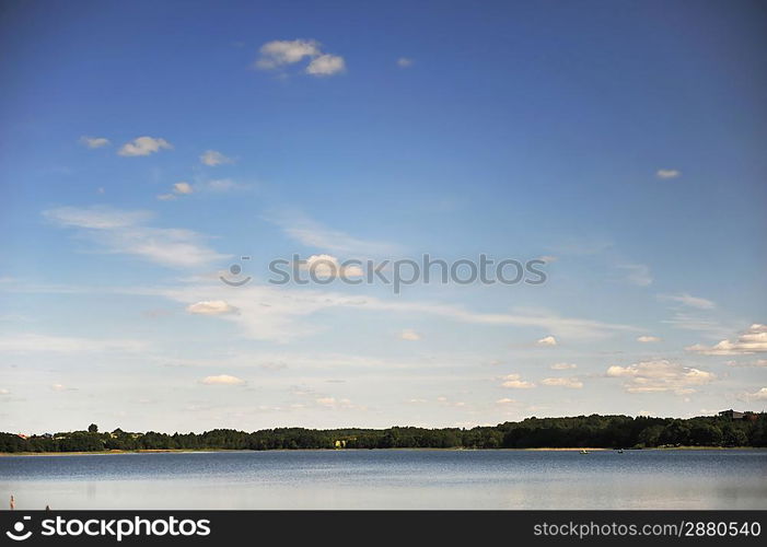 calm water of lake, woods on other side and blue sky. landscape