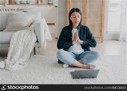 Calm woman practices yoga, meditates to relaxing music on laptop. Stress relief, healthy lifestyle at home.