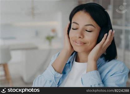 Calm young female wearing wireless headphones listening to relaxing music, enjoying sound at home. Happy woman listens to audio affirmations or meditation, resting with closed eyes at home.. Female wearing wireless headphones listening to relaxing music or meditation, enjoying sound at home