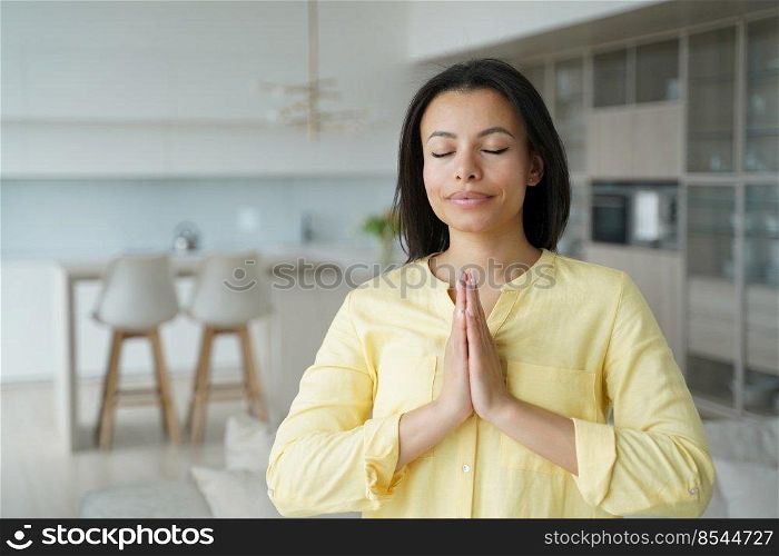 Calm young woman folded hands in namaste gesture, praying with closed eyes at home. Female practice yoga, meditating, breathing, relax her mind. Healthy lifestyle, anti-stress meditation.. Calm woman makes namaste gesture, practice yoga at home. Healthy lifestyle, anti-stress meditation