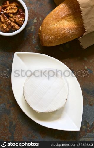Camembert cheese on small plate with baguette and walnuts on the side, photographed overhead on slate with natural light