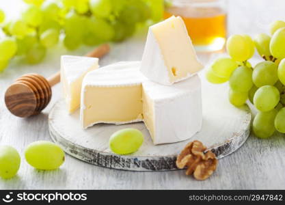 camembert cheese with grapes, honey and nuts on wooden background