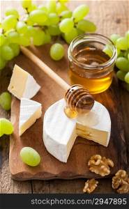 camembert cheese with grapes, honey and nuts on wooden background