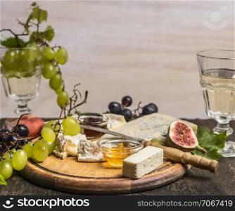 Camembert, Dor Blue, Gorgonzola, honey, grapes and wine on a cutting board on wooden rustic background top view close up