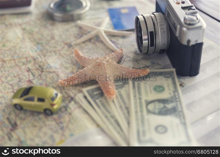camera, compass, passport, credit card, banknote money, globe, map, car and starfish figurine on wooden table for use as traveling concept (vintage tone and selected focus)
