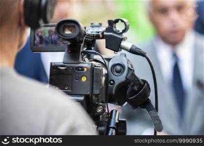Camera operator working at a press conference outdoors. Journalists interviewing formal dressed politician or businessman at a media event. 