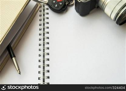 Camera, white notebook, pen and car key placed on the desk
