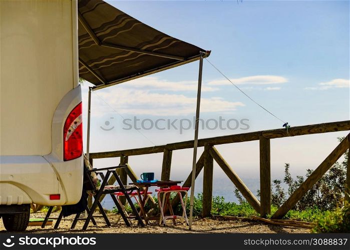 Camper vehicle with roll out awning and tourist table with chairs on spanish sea coast. Camping on seaside. Holidays and travel with motor home.. Camper and chairs on sea shore