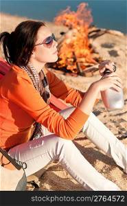 Camping happy woman sitting by campfire relaxing on beach
