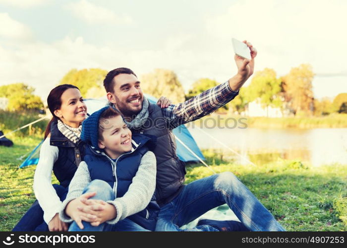 camping, hike, technology and people concept - happy family with smartphone taking selfie at campsite. family with smartphone taking selfie at campsite