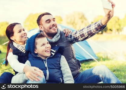 camping, hike, technology and people concept - happy family with smartphone taking selfie at campsite. family with smartphone taking selfie at campsite