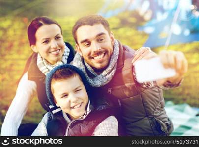 camping, hike, technology and people concept - happy family with smartphone taking selfie at campsite. family with smartphone taking selfie at campsite