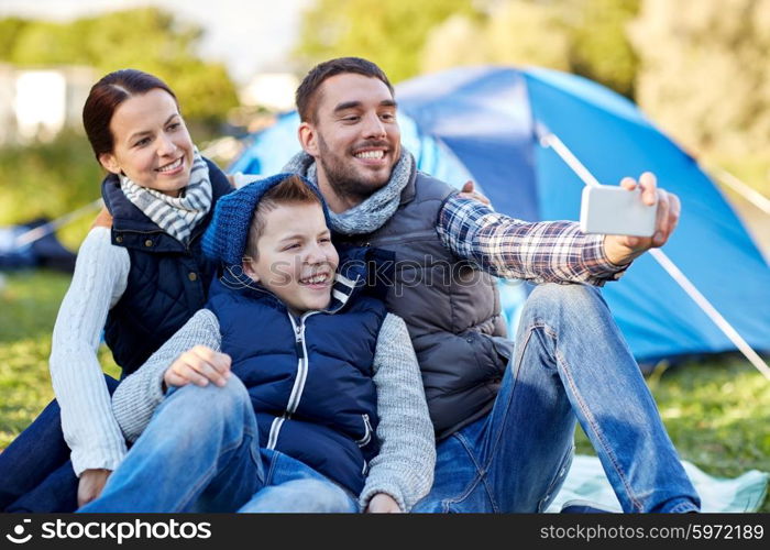 camping, hike, technology and people concept - happy family with smartphone taking selfie at campsite