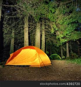 Camping in the forest. Orange illuminated tent under dark night trees