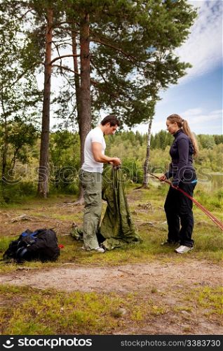 Camping lifestyle - a man and woman setting up a tent by a lake