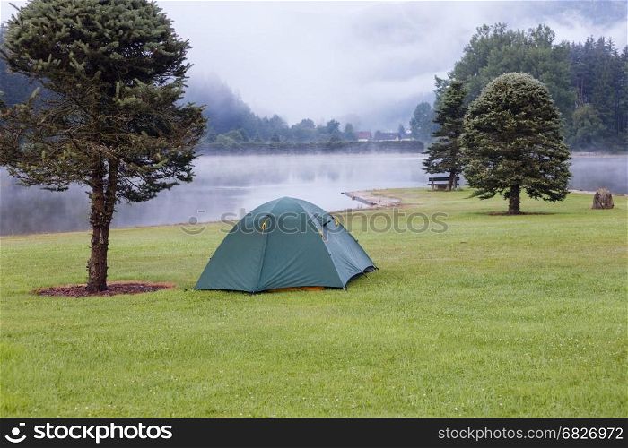 Camping tent on green grass lawn near the lake