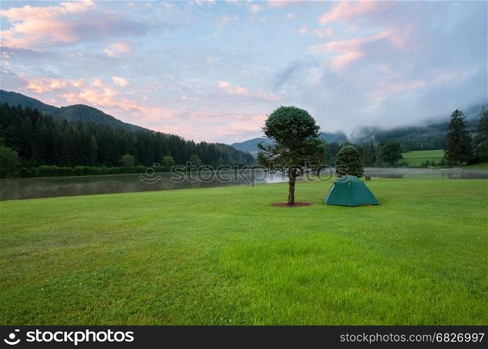 Camping tent on green grass lawn near the lake