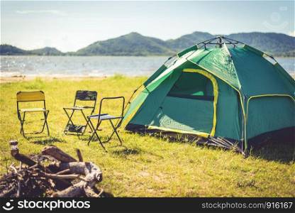 Camping tent with extinguished bonfire in the green field meadow, Lake and mountain background. Picnic and travel concept. Nature theme.