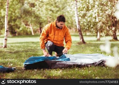 camping, tourism and concept - man setting up tent outdoors. man setting up tent outdoors