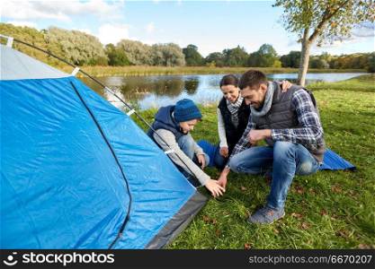 camping, tourism and family concept - happy mother, father and son setting up tent at campsite. happy parents and son setting up tent at campsite. happy parents and son setting up tent at campsite