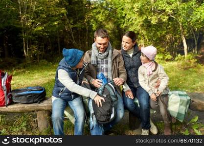 camping, tourism and family concept - happy mother, father, son and daughter with backpacks and thermos at camp in woods. happy family with backpacks and thermos at camp. happy family with backpacks and thermos at camp