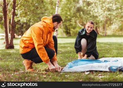 camping, tourism and travel concept - happy couple setting up tent outdoors. happy couple setting up tent outdoors