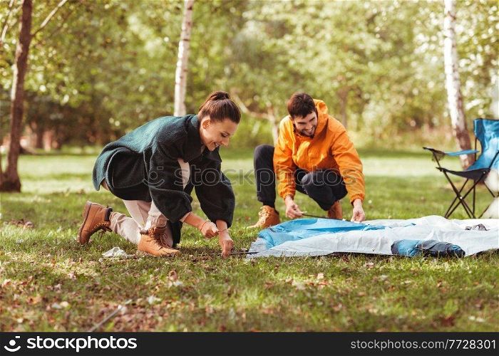 camping, tourism and travel concept - happy couple setting up tent outdoors. happy couple setting up tent outdoors