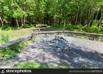 camping, tourism, hike and environment concept - camp fire place with bench seats in forest