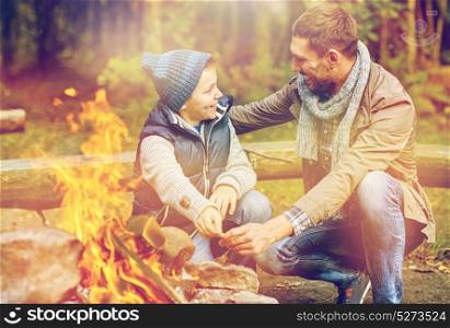 camping, tourism, hike and family concept - happy father and son roasting marshmallow over campfire. father and son roasting marshmallow over campfire