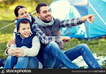 camping, tourism, hike and people concept - happy family over tent at camp site pointing finger to something