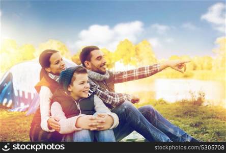 camping, tourism, hike and people concept - happy family over tent at camp site pointing finger to something. happy family with tent at camp site