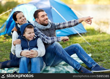 camping, tourism, hike and people concept - happy family over tent at camp site pointing finger to something