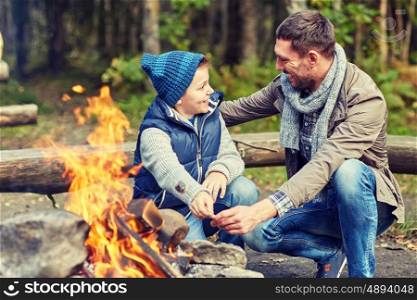 camping, tourism, hike, family and people concept - happy father and son roasting marshmallow over campfire
