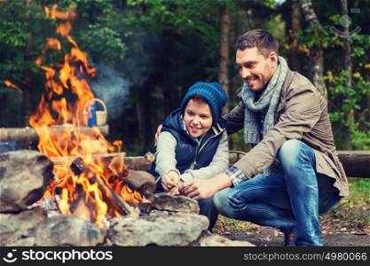 camping, tourism, hike, family and people concept - happy father and son roasting marshmallow over campfire. father and son roasting marshmallow over campfire