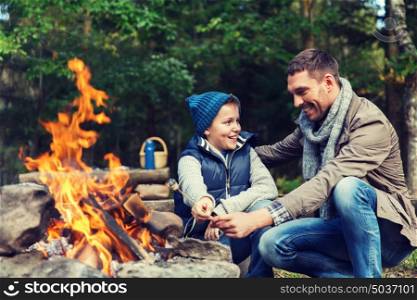 camping, tourism, hike, family and people concept - happy father and son roasting marshmallow over campfire. father and son roasting marshmallow over campfire