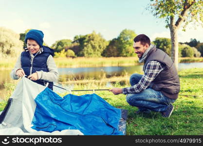 camping, tourism, hike, family and people concept - happy father and son setting up tent outdoors. happy father and son setting up tent outdoors