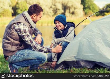 camping, tourism, hike, family and people concept - happy father and son setting up tent outdoors. happy father and son setting up tent outdoors
