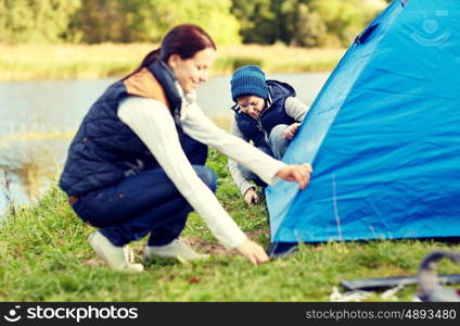 camping, tourism, hike, family and people concept - happy mother and son setting up tent outdoors