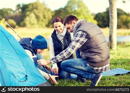 camping, tourism, hike, family and people concept - happy parents and son setting up tent outdoors