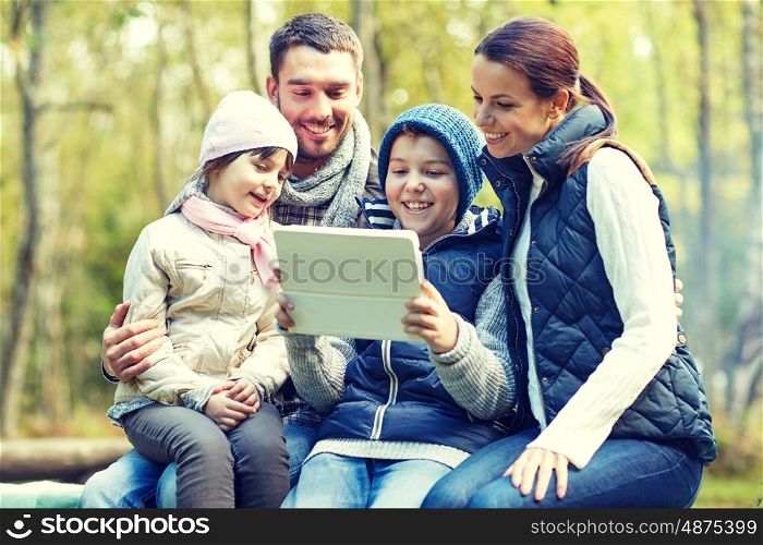camping, tourism, hike, technology and people concept - happy family sitting on bench with with tablet pc computer at camp in woods