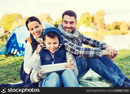 camping, tourism, hike, technology and people concept - happy family with tablet pc computer and tent at camp site. happy family with tablet pc and tent at camp site