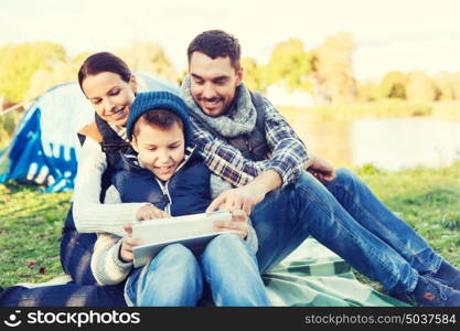 camping, tourism, hike, technology and people concept - happy family with tablet pc computer and tent at camp site. happy family with tablet pc and tent at camp site