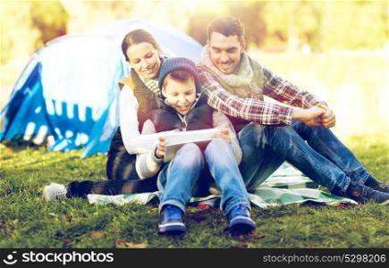 camping, tourism, hike, technology and people concept - happy family with tablet pc computer and tent at camp site. happy family with tablet pc and tent at camp site