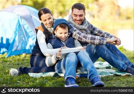 camping, tourism, hike, technology and people concept - happy family with tablet pc computer and tent at camp site