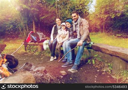 camping, travel, tourism and hike concept - happy family sitting on bench and talking at camp near campfire in woods. happy family sitting on bench at camp fire
