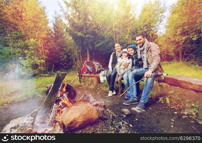 camping, travel, tourism and hike concept - happy family sitting on bench and talking at camp near campfire in woods. happy family sitting on bench at camp fire