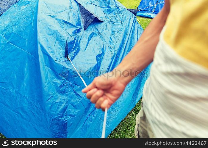 camping, travel, tourism, hike and people concept - close up of man setting up tent outdoors