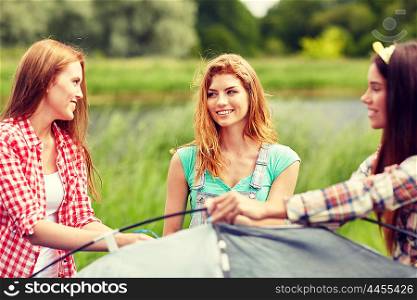 camping, travel, tourism, hike and people concept - group of smiling friends setting up tent outdoors